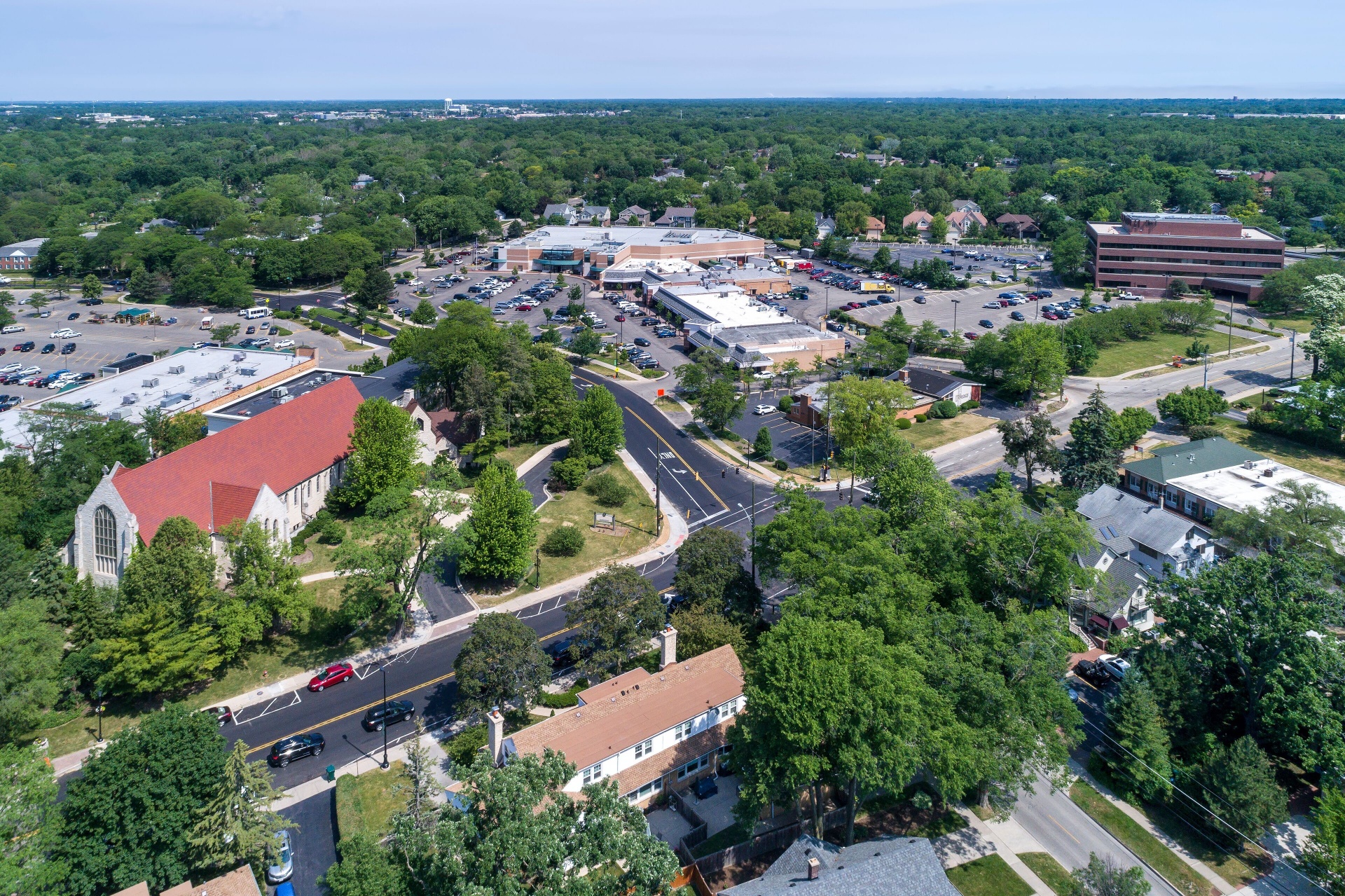 Aerial view of a North Shore downtown — tree-lined streets, a stone church, and the village commercial core surrounded by mature canopy